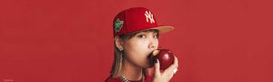 Woman biting into an apple wearing a red New York Yankees cap in front of a red background